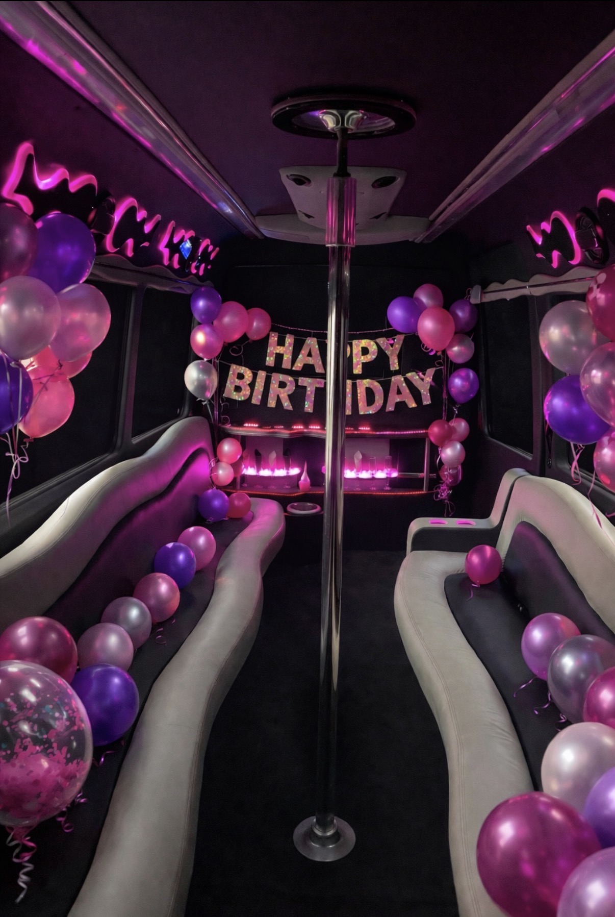 Party bus interior decorated with pink and purple balloons and a HAPPY BIRTHDAY banner