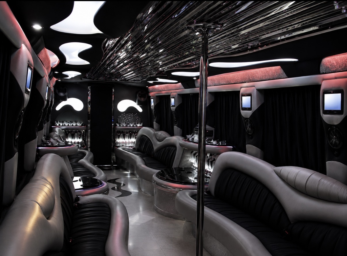 Luxury party bus interior with pole, seating, bar, and flat-screen televisions