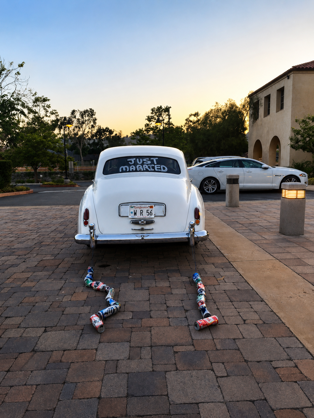 Vintage white Bentley wedding getaway car with Just Married window paint and tin cans trailing at sunset